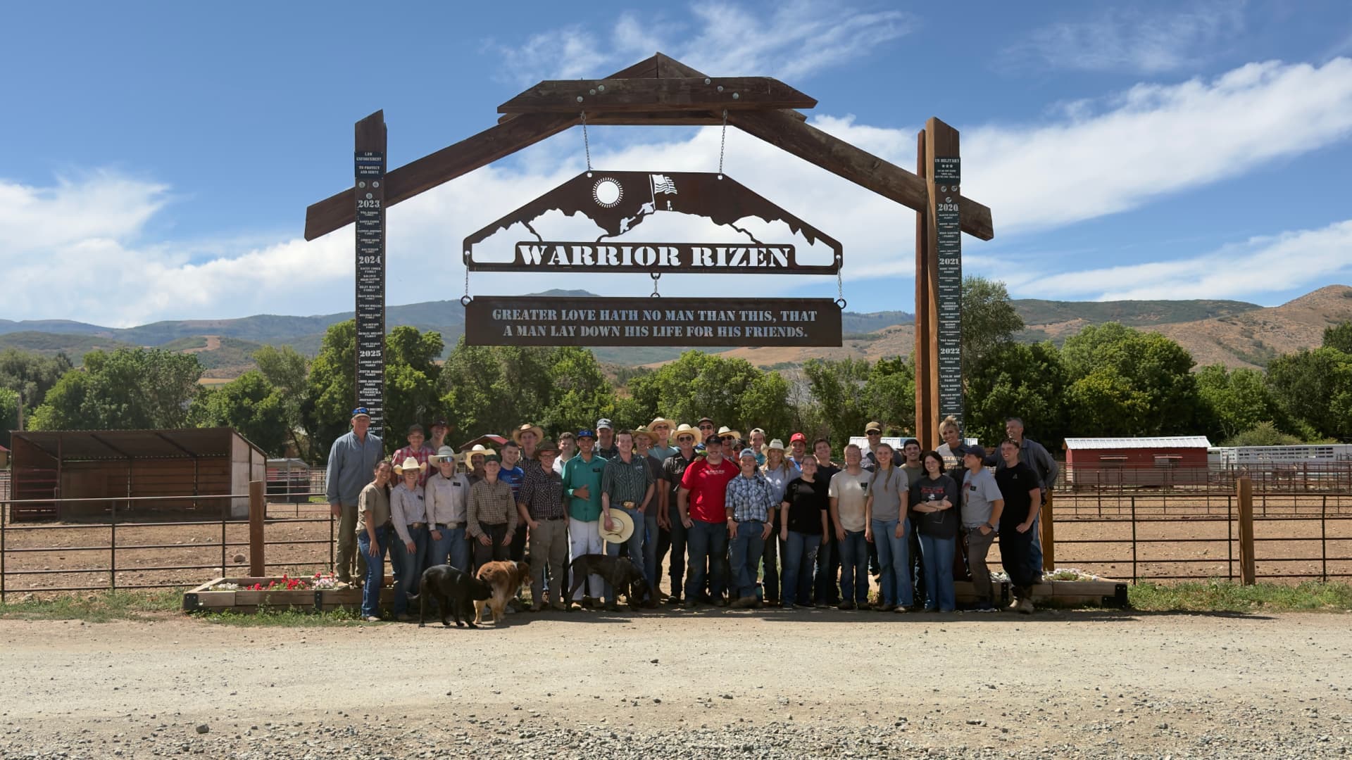 Volunteers and community members gathered beneath the Warrior Rizen ranch entrance sign on a sunny day.