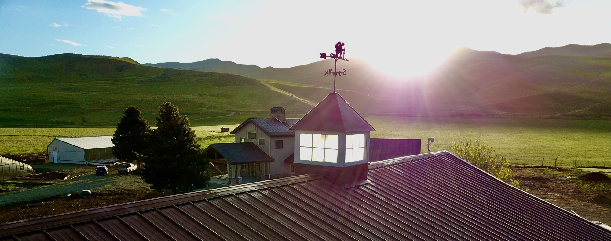 Sunrise over Warrior Rizen Ranch, with the barn cupola, ranch buildings and green hills.